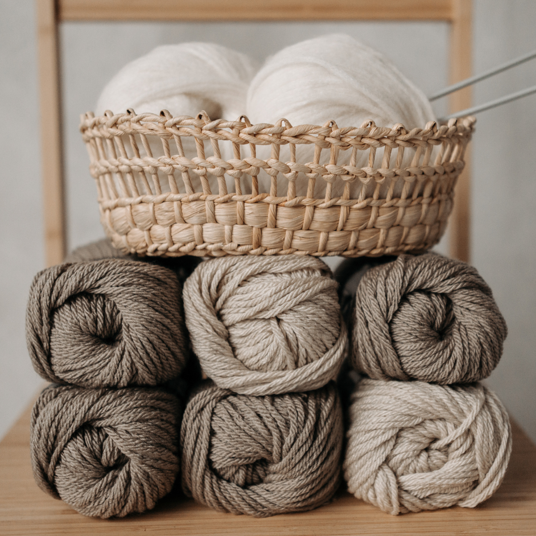 Basket with white yarn and stack of beige yarn balls on a wooden surface