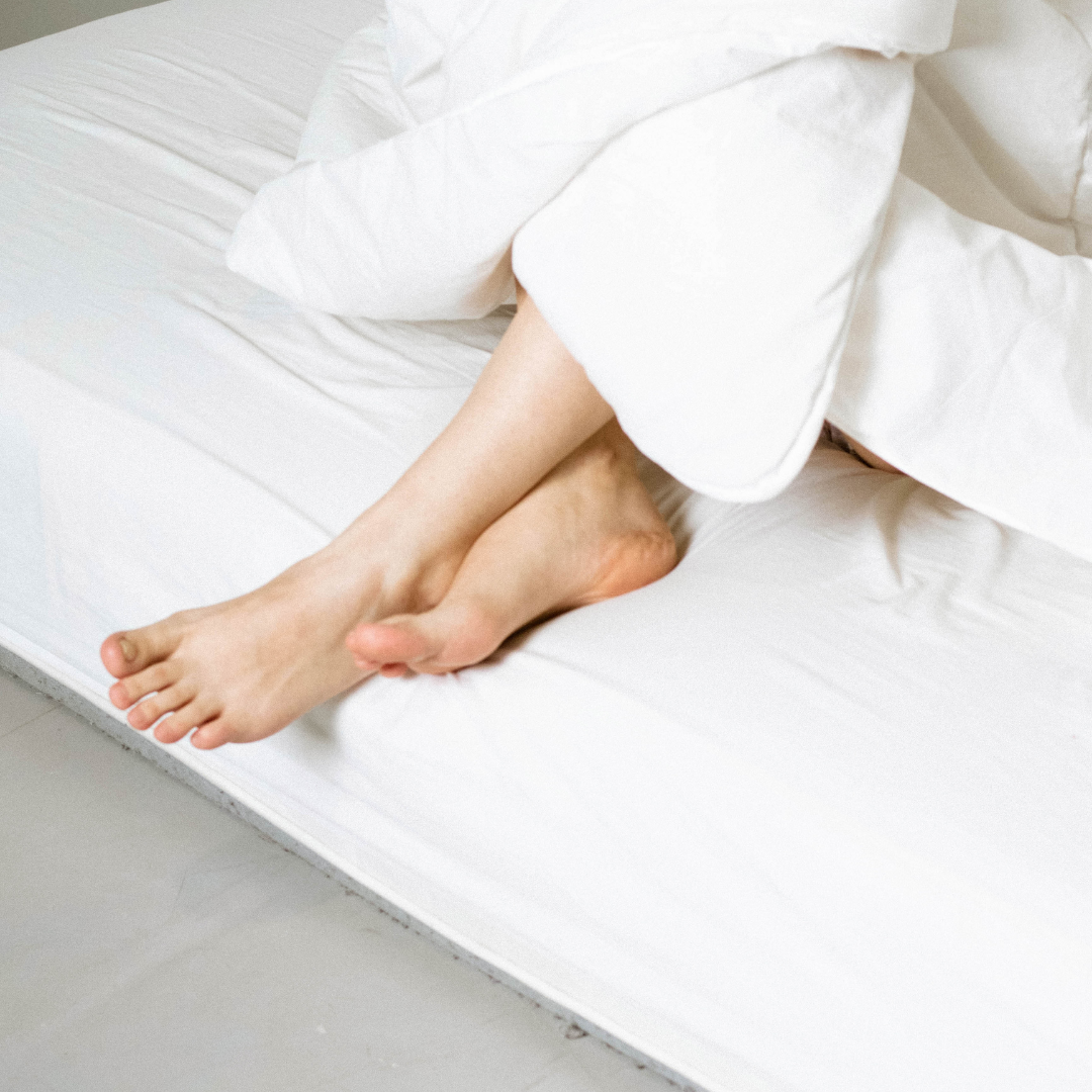 Person lying on a white mattress with white bedding