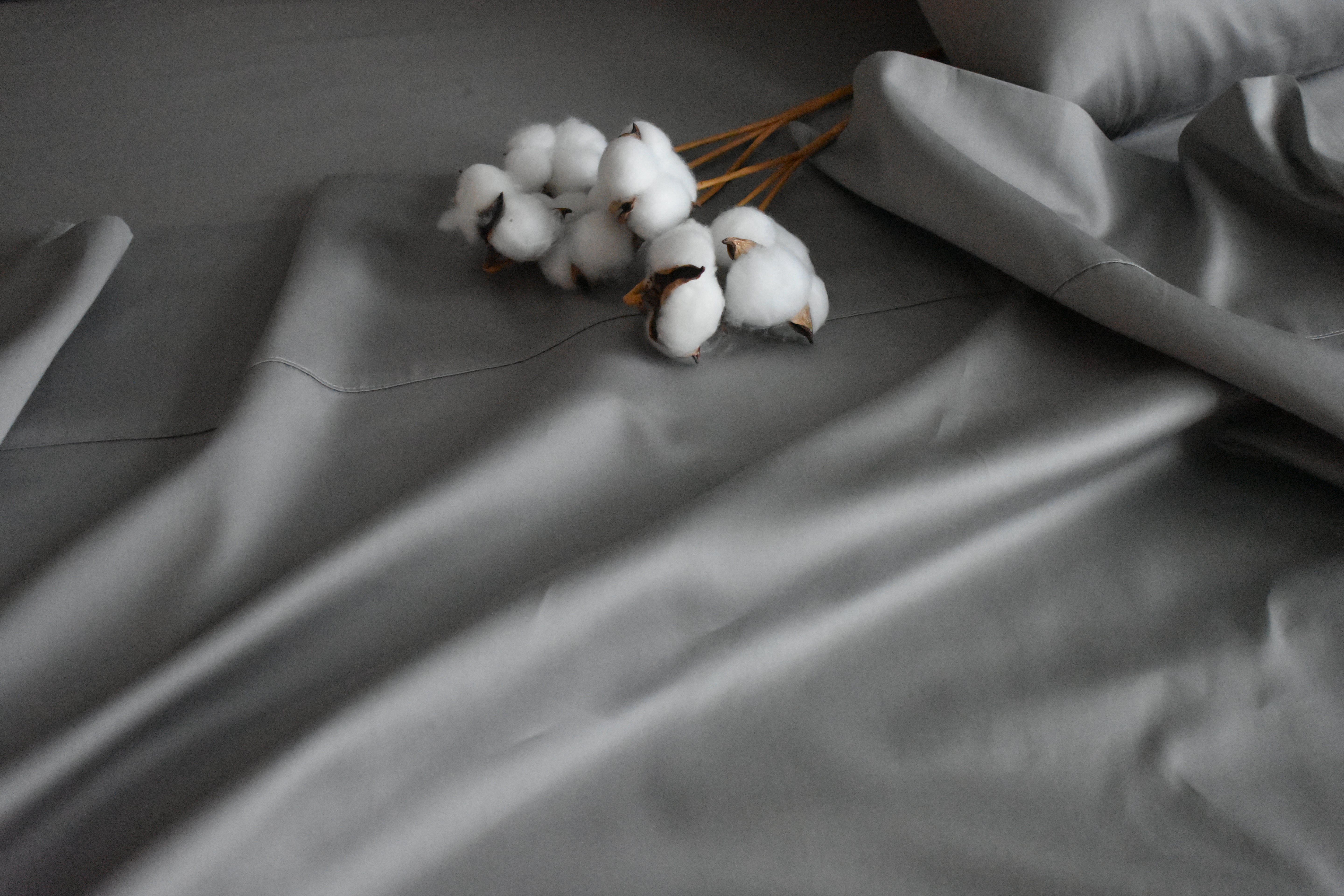 Gray bedsheet on a bed in flowy pattern and decorated with cotton buds with brown stems on top.