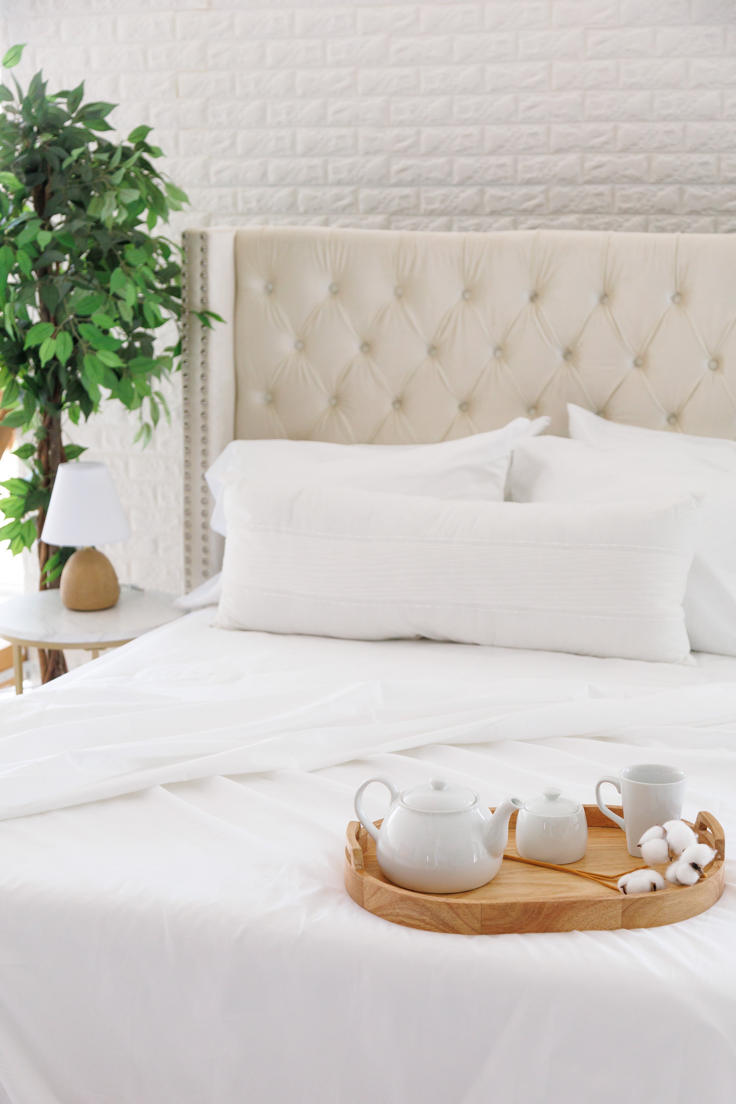 Cream headboard bed with white cotton sateen sheets, decorated with a tray holding a coffee kettle, cups, and an open book on the bed.