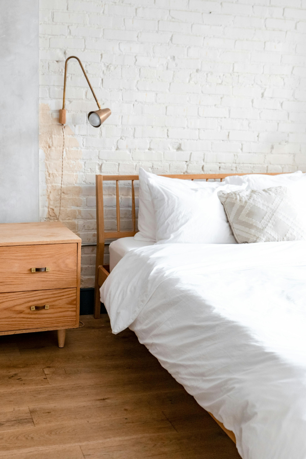 Bedroom with wooden bed, nightstand, and white brick wall.