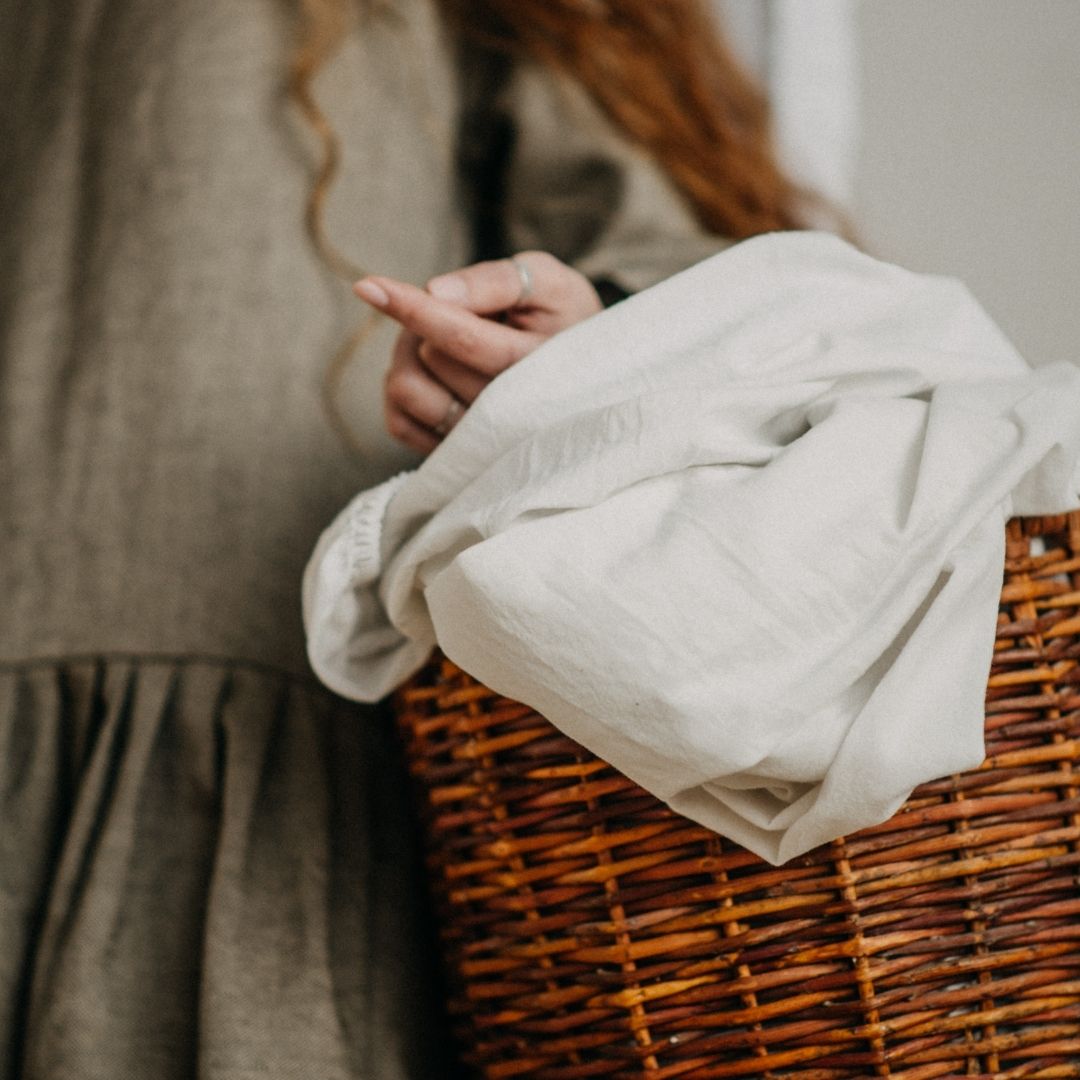 Person holding a white sheets over a wicker basket with a neutral background