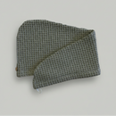 A Trees & hugs Sage green Waffle hair wrap with a coconut shell button and white loop, folded neatly on a solid gray background.