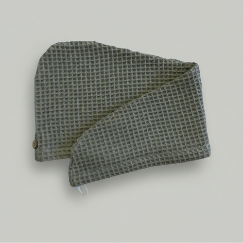 A Trees & hugs Sage green Waffle hair wrap with a coconut shell button and white loop, folded neatly on a solid gray background.