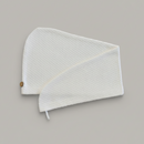 A Trees & hugs white textured hair wrap with a coconut shell button and white loop, folded neatly on a solid gray background.