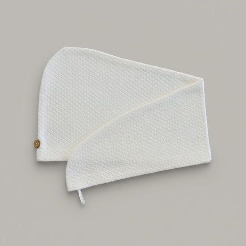 A Trees & hugs white textured hair wrap with a coconut shell button and white loop, folded neatly on a solid gray background.
