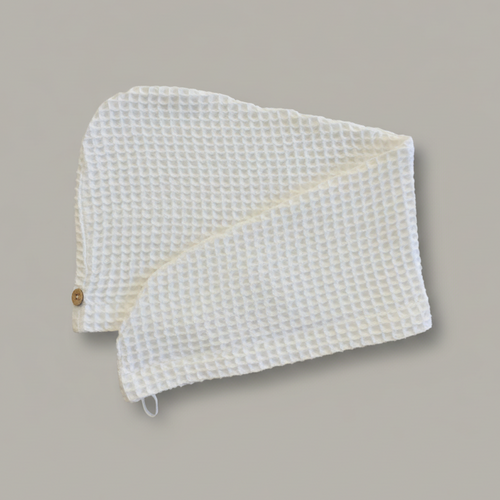 A Trees & hugs White Waffle hair wrap with a coconut shell button and white loop, folded neatly on a solid gray background.