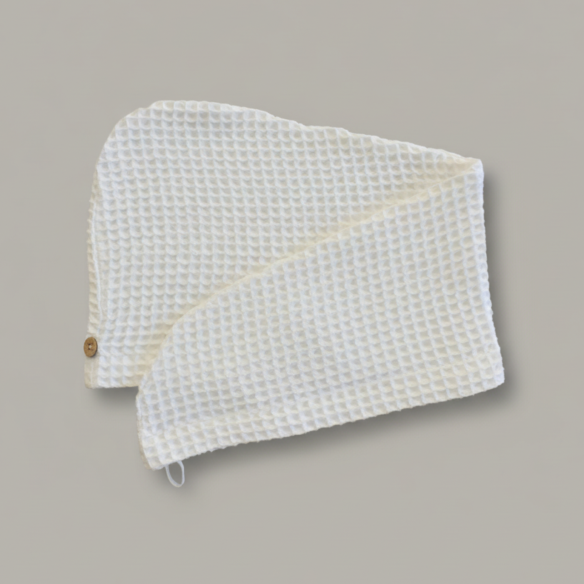 A Trees & hugs White Waffle hair wrap with a coconut shell button and white loop, folded neatly on a solid gray background.